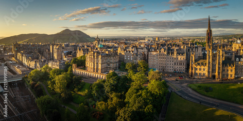 Aerial view of the historic Edinburgh skyline at sunset, featuring stone buildings, lush parks, and railway tracks, with Arthur's Seat in Edinburgh, Scotland, United Kingdom.
