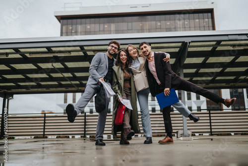 Four business colleagues smile and pose together outdoors on a rooftop. A joyful professional team stands arm in arm in an urban rooftop setting.