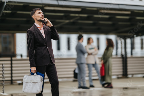 Canvas Print A businessman stands outdoors talking on a mobile phone while holding a briefcase