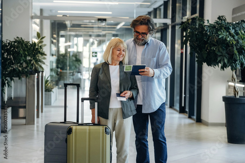 Bild auf Leinwand Senior couple with luggage standing inside a modern hotel lobby, checking travel