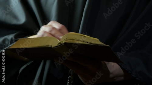 Monk slowly turns book pages while reading in dim dramatic light