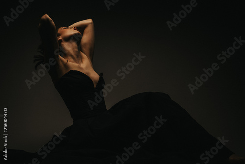 Foto Woman wearing an elegant black dress poses with her arms raised in a dark studio