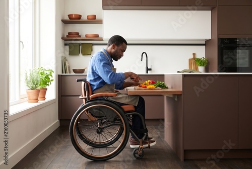 Man in a wheelchair cooking a meal at the lowered counter of his bright accessible kitchen