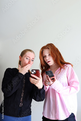 Obraz na płótnie Two women shocked by smartphone content, reacting to news or message, emotion and communication concept