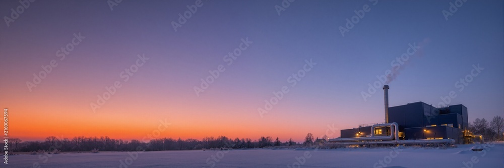 Fototapeta premium City heating plant at sunset in winter. Industrial thermal power station in a snowy landscape. Wide banner format