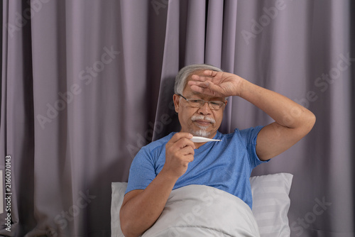 Canvas Print Exhausted senior man feeling miserable and sick with high fever holding thermome