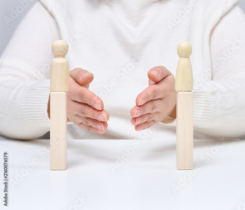 Bild auf Leinwand A man uses his hands to bring together two wooden figures on stands, symbolizing negotiators