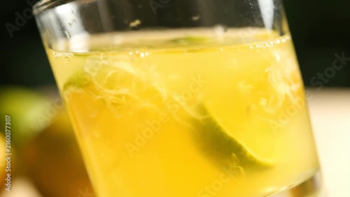 Close-up of a Vibrant Yellow Citrus Cocktail or Refreshing Drink Served in a Glass with Submerged Fresh Lime Slices and Bubbly Liquid