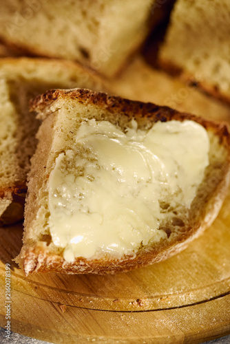 Close-up of freshly baked artisan sourdough bread sliced on a round wooden board. A slice topped with butter in the foreground, rustic food styling.