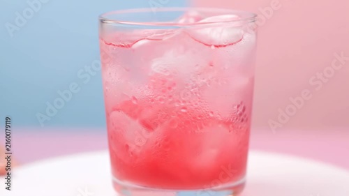Vibrant pink soda or cocktail in a clear glass with abundant ice and heavy condensation, highlighting refreshing coolness against a bright pastel bi-color background.