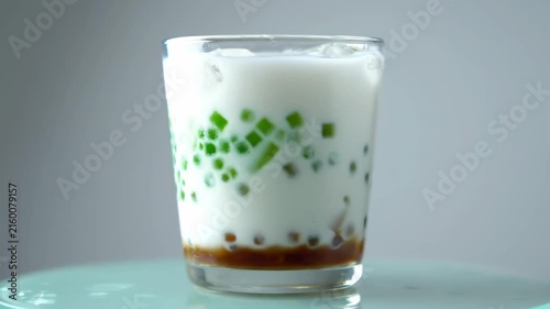 Close-up of tropical Asian dessert drink with green jelly cubes, coconut milk, and palm sugar syrup being served in a glass