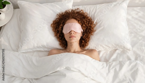 Young woman with curly hair sleeping in bed wearing a pink eye mask