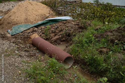 Картината върху платно Underground drainage tube partially covered with soil in ditch outdoors, pipeline backfilling process, earthworks improvement, construction phase