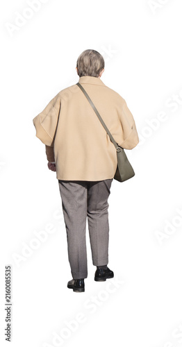 Femme âgée vue de dos marchant avec un sac à bandoulière, vêtue d’un manteau beige, d’un pantalon gris et de chaussures noires