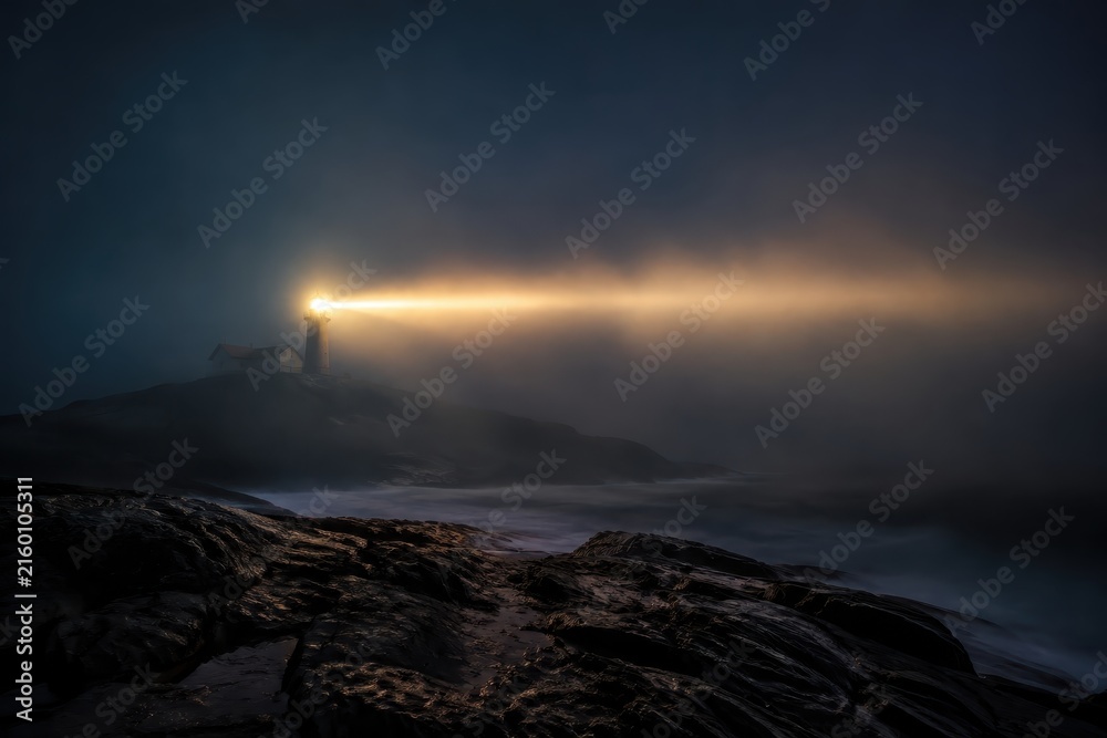 Fototapeta premium Lighthouse beam sweeping through thick sea fog at night