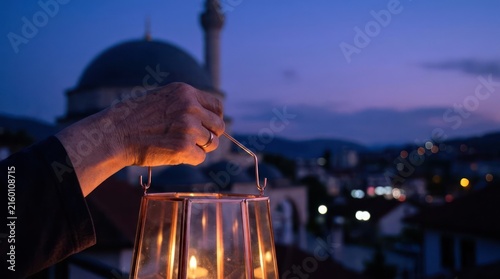 Person holding lantern near mosque at night.