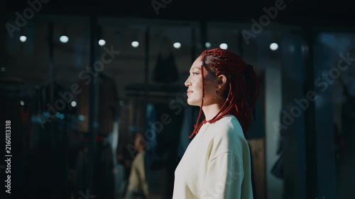 Woman with red braided hair looking thoughtfully at storefront in modern city at night