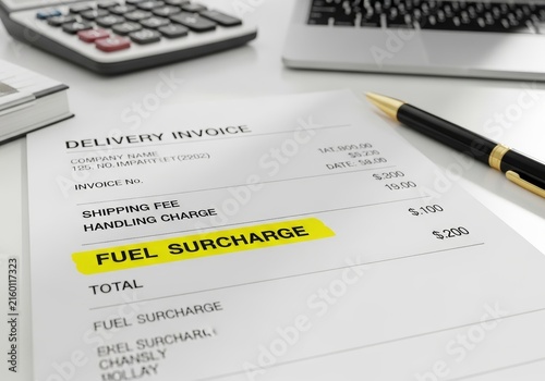 Delivery invoice with highlighted fuel surcharge on paper document. Business financial bill with calculator and pen on desk. Concept of logistics cost, shipping fee and accounting.