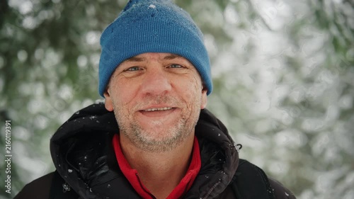 Close up of a bearded man smiling in a snowy forest wearing a blue beanie and winter coat