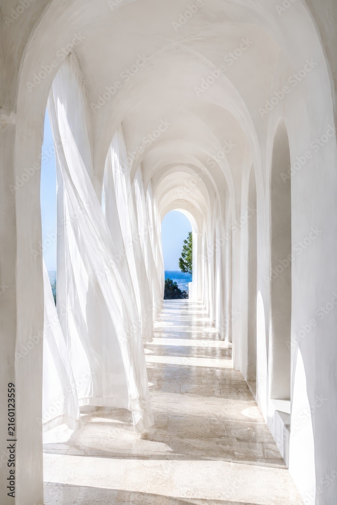 Fototapeta premium White arched corridor with sheer curtains at seaside villa