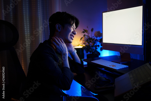Fotografie Young Asian man easing neck pain after prolonged computer work at night