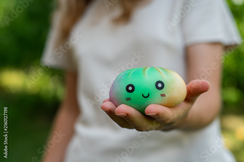 Child holding a green kawaii dumpling squishy toy outdoors.