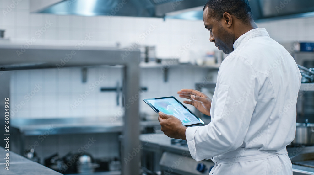 Fototapeta premium Head chef reviewing AI kitchen efficiency dashboard in restaurant