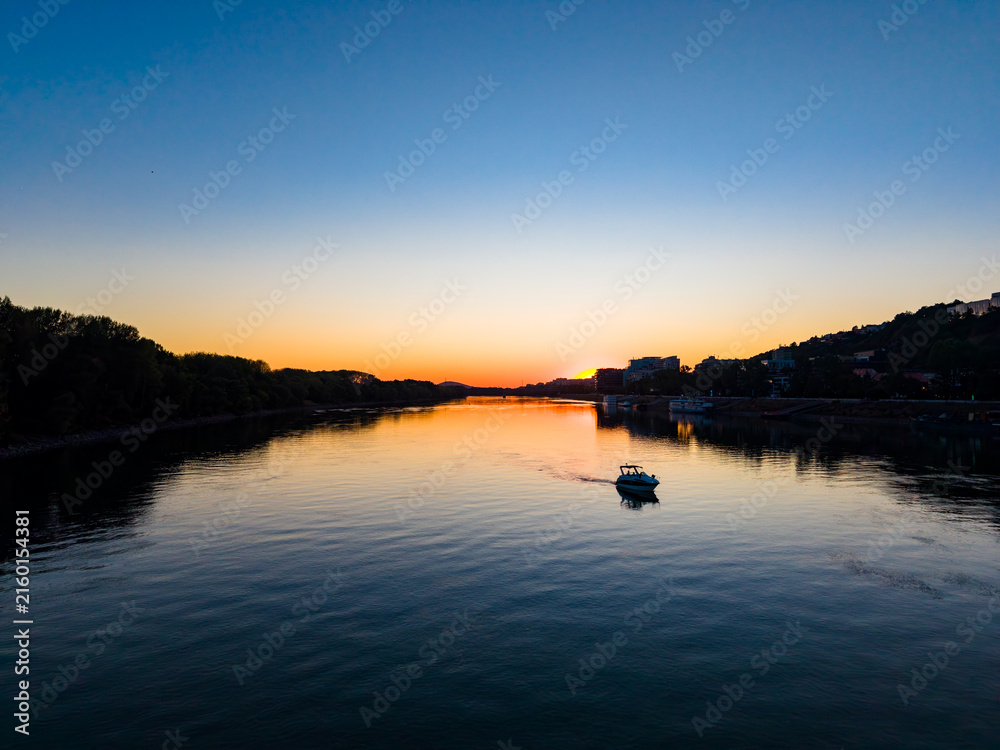 Obraz premium Sunset over the river with a boat sailing in the calm waters near the shoreline