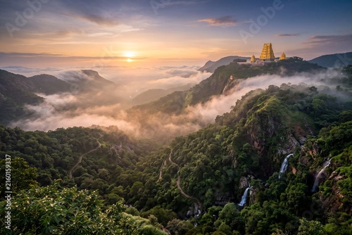 Breathtaking aerial view of winding ghat roads on lush green misty mountains leading to a sacred temple, hyper-realistic digital landscape