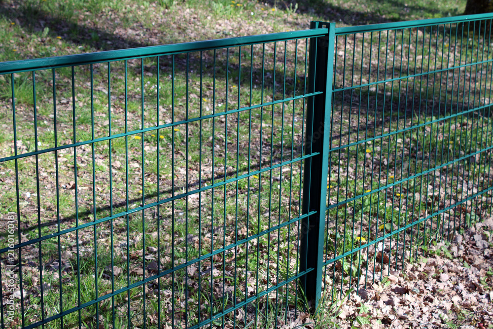 Fototapeta Clôture en panneaux de grillage rigide à double fil de couleur verte, installée sur des poteaux métalliques pour délimiter un espace extérieur.