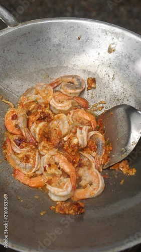Cooking Thai stir-fried prawns with holy basil (Phad Kra Pao Goong). Searing prawns in a wok with garlic and chilies, seasoning, and tossing with fresh basil.