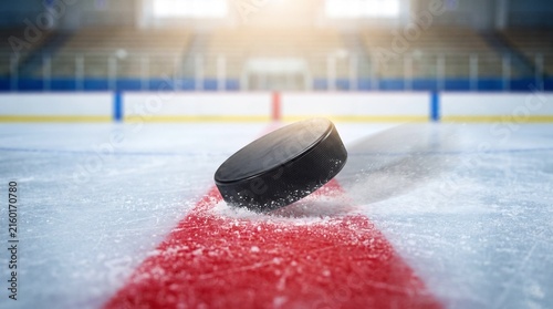 Ice hockey puck on red line under bright indoor lights  