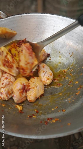 Cooking Thai stir-fried chicken wings with sweet basil (Peek Gai Phad Bai Horapha). Sautéing pounded garlic and red chilies in oil, adding chicken wings, simmering with a splash of water