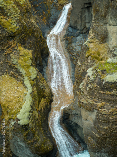 Waterfall cascading through a rugged moss-covered canyon in Iceland
