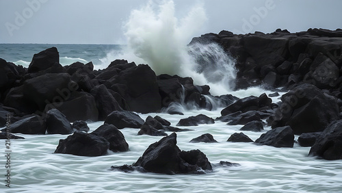 Jagged sea rocks during a storm with a crashing wave and white spray.