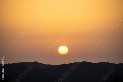 Obraz na plátne A clear, bright sun with a visible sunspot sets over a dark silhouetted horizon