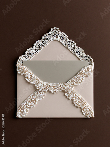 Elegant Lace Envelope: A delicate, open envelope adorned with intricate white lace trim, holding a plain grey insert, presented against a rich brown background.