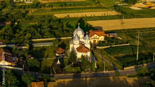 Aerial view of an Orthodox church with a silver dome surrounded by green fields and rural houses in Deva, Hunedoara, Romania.