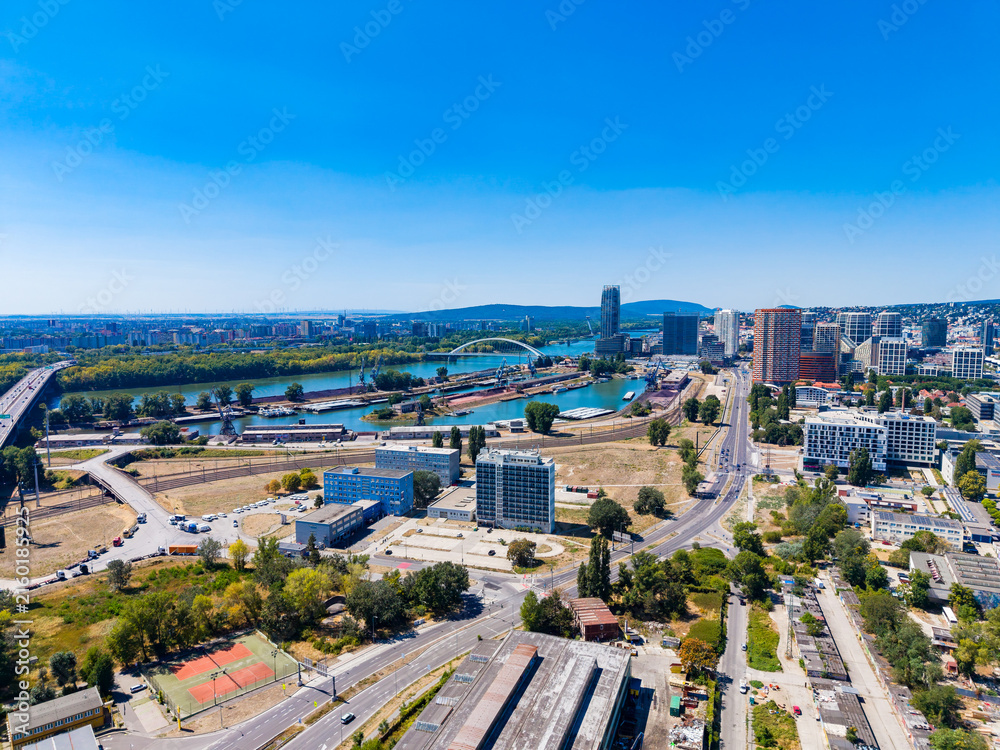 Fototapeta premium View of a city area with buildings, a river, and roads under a clear sky, showing urban development and open spaces
