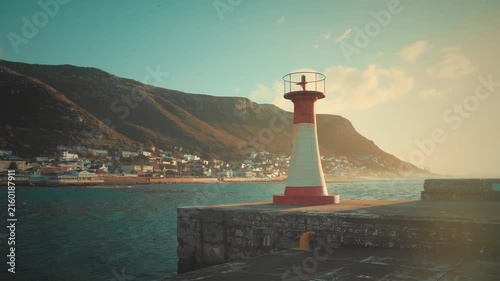 Red and White Lighthouse on Concrete Pier at Sunset, Coastal Town with Mountains in Background, Cape Town, South Africa