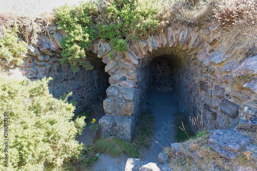 Obraz na plátně A weathered stone structure features two archways leading into dark tunnels, wit