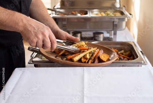 Caterer serving roasted vegetables on a ceramic platter
