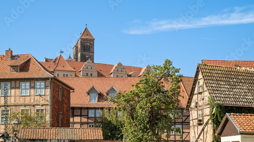 Traditional half-timbered houses with red tiled roofs in the historic old town of Quedlinburg, Germany. The towers of St. Servatius Church stand out against a clear blue summer sky in Saxony-Anhalt.