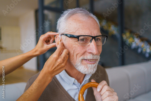 Close up of female hand with hearing aid and senior man , assistive listening device for elderly patient, hearing care, healthcare support and rehabilitation concept