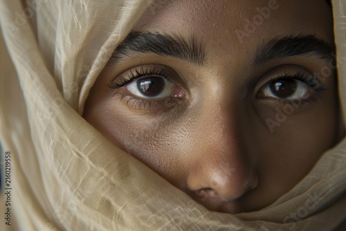 Close up portrait of a young muslim woman with brown eyes wearing a beige veil, symbolizing modesty and religious observance