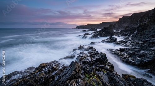 Scenic long exposure of a rugged rocky coastline at twilight with misty ocean waves and dramatic sky