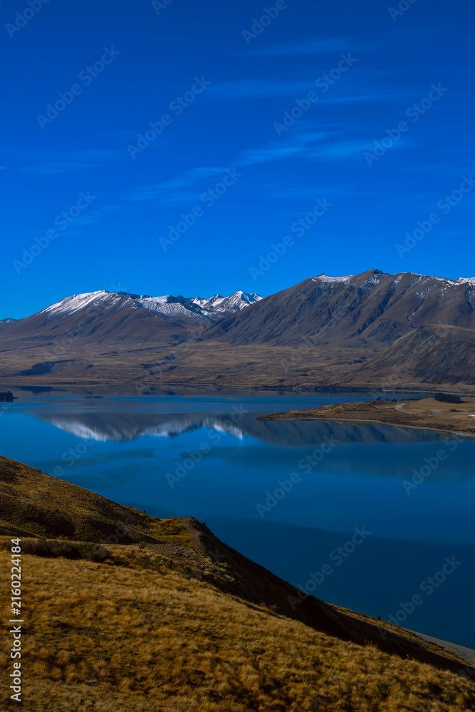 Fototapeta premium Lake Tekapo with snow-capped Southern Alps and dramatic blue sky, New Zealand