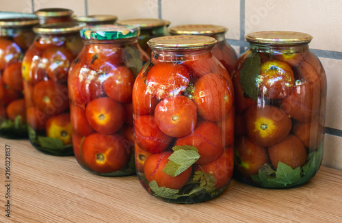 Jars of pickled tomatoes with herbs on wooden table