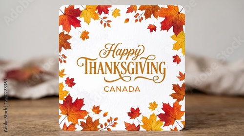 A festive happy thanksgiving canada greeting card decorated with colorful autumn leaves on a rustic wooden table background