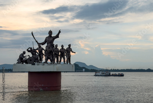 Statue of Lachit Borphukan and his soldiers stands in the Brahmaputra River as a passenger ferry sails past during sunset